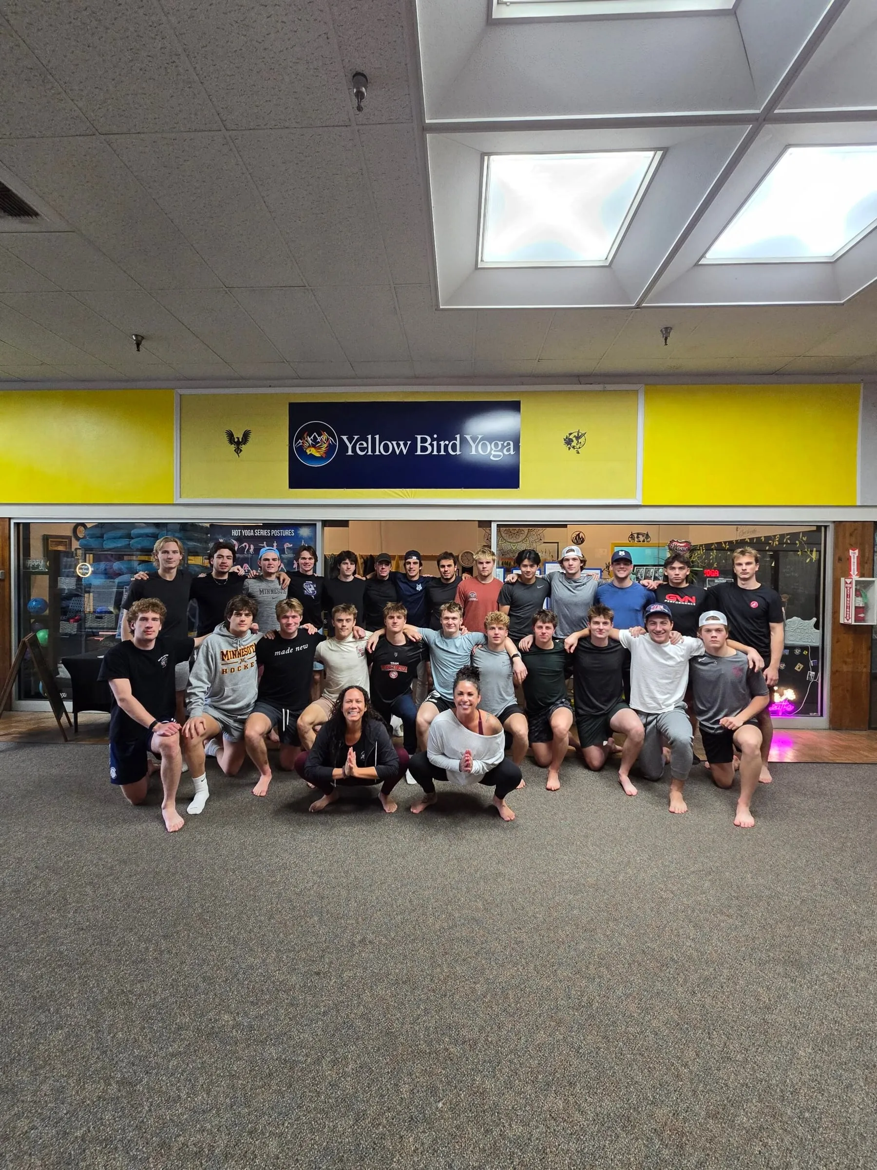 A large group gathered for a photo under the Yellow Bird Yoga sign
