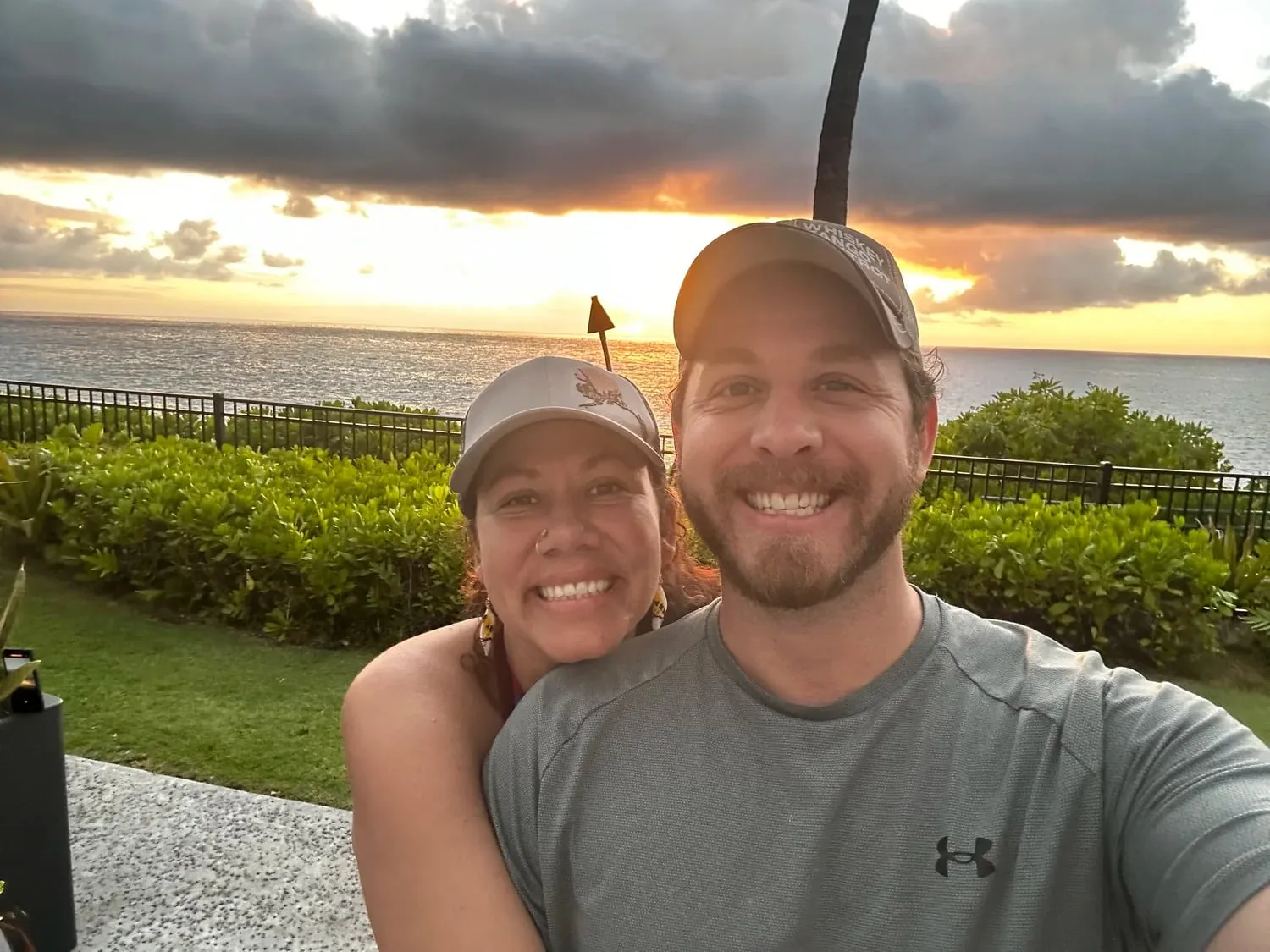 Two people smiling together in front of a sunset over the ocean