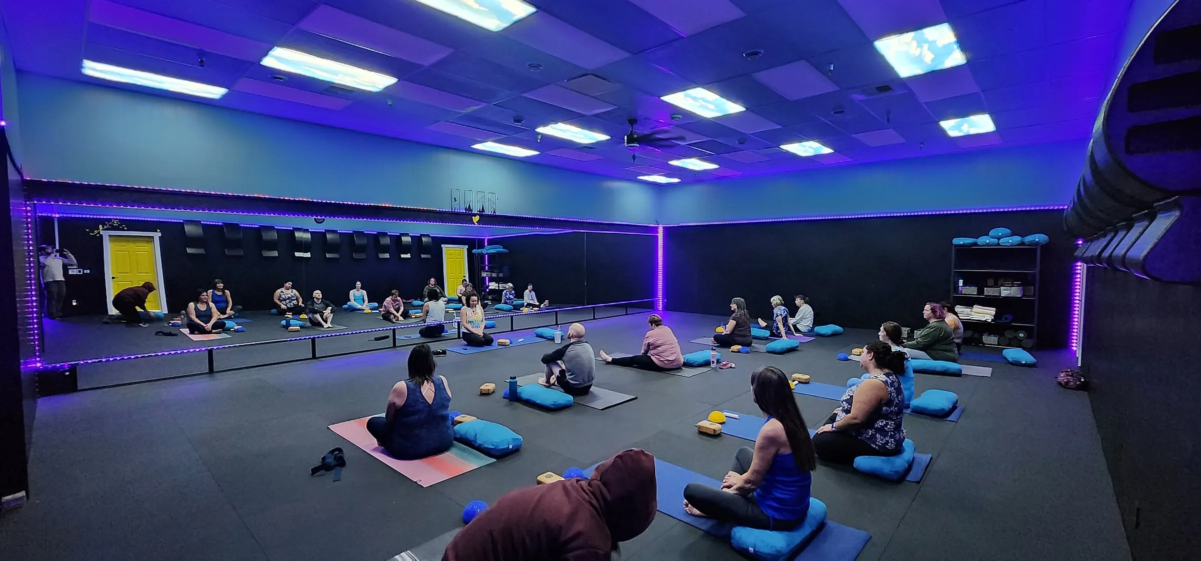 Women seated on mats in the studio under purple and blue lights